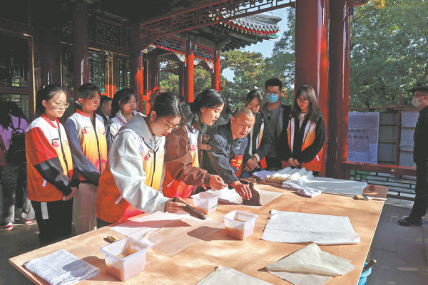 Students try paperhanging, an ancient technique used in traditional Chinese architecture, on the open day of the Summer Palace in Beijing to mark end of the restoration of Jingfu Ge on Oct 30.JIANG DONG/CHINA DAILY