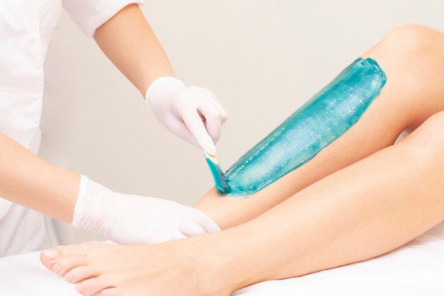 azulene depilation. wax hair removal, shugaring. concept of smooth skin without hair. azulene of green color. the master puts azulene on the girls legs