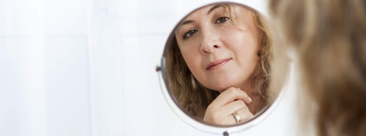 beauty concern - woman looking in mirror in middle age with aging skin