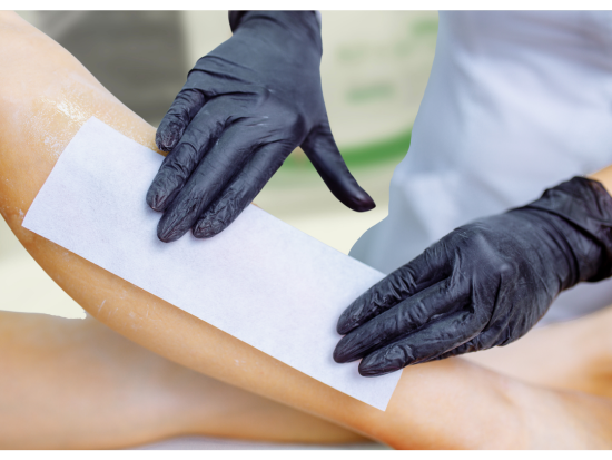 Waxologist applying cotton strip on model’s leg, who is on an examination table