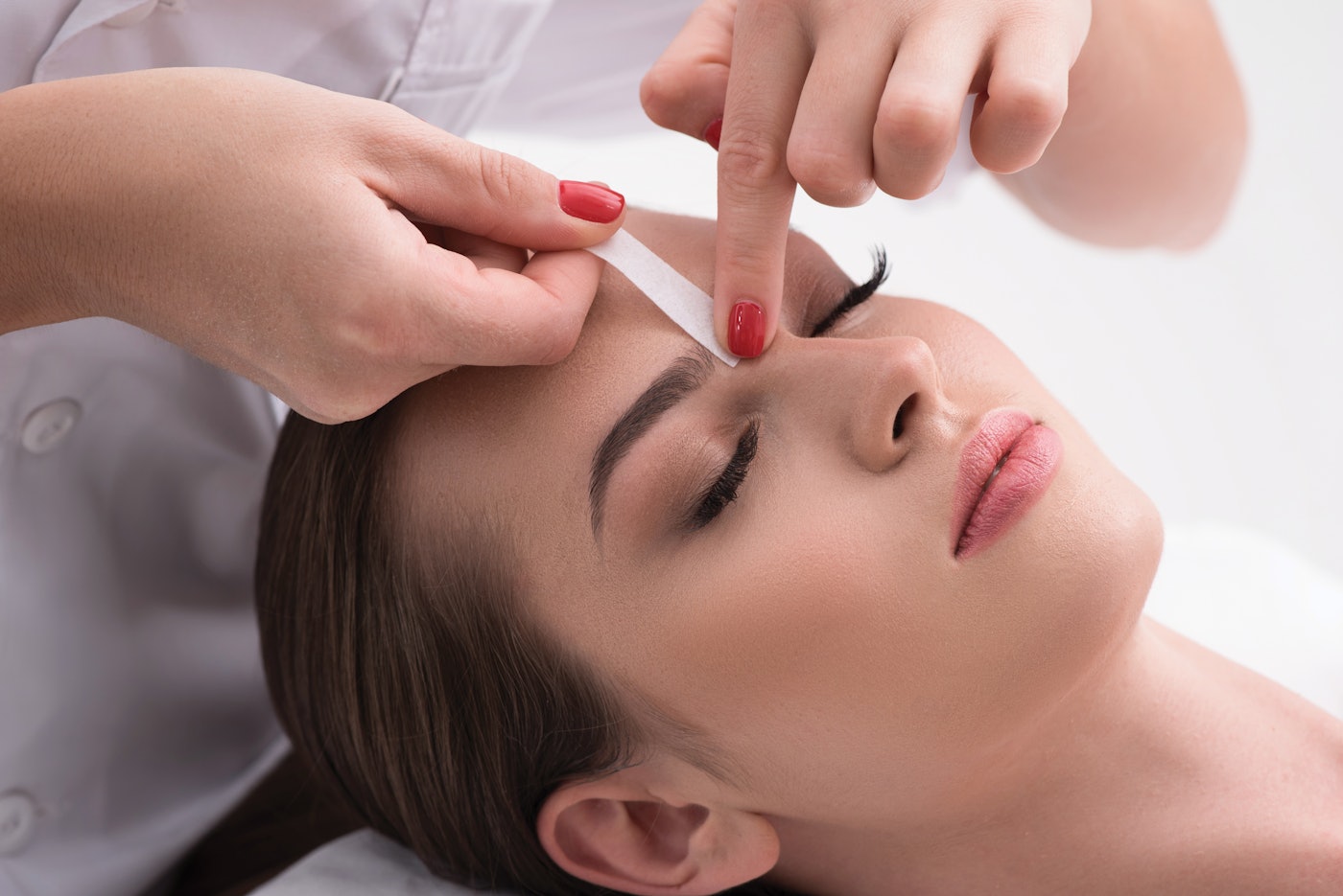 Already perfect. Close up of hands waxing beautiful woman eyebrow, lying in beauty salon with closed eyes isolated on white background